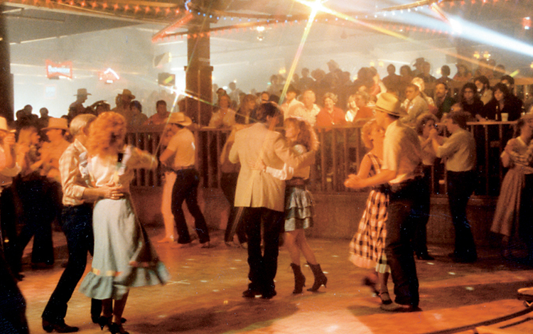 People square dancing on lively dance floor in front of onlookers.